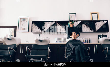 Donna seduta sulla sedia del salone mentre un hair stylist lavare i capelli. Parrucchiere tergi i capelli asciutti utilizzando un asciugamano nella vasca di lavaggio. Foto Stock