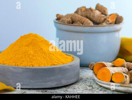 Composizione di curcuma utilizzato come spezia in cucina e di heath vantaggi ciotola di argilla con luce sfondo blu il fuoco selettivo per aggiungere spazio di copia Foto Stock