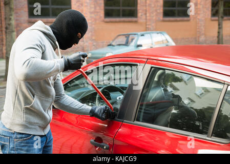 Ladro in giacca con cappuccio e Balaclava apertura auto della porta con palanchino Foto Stock