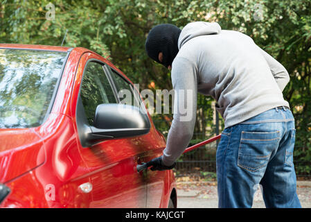 Ladro in giacca con cappuccio e Balaclava apertura auto della porta con palanchino Foto Stock