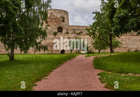 Un antico muro di fortificazione con torri di avvistamento. prima che il muro cresce un albero a foglie decidue con una corona circolare. russia, Pskov Regione Foto Stock