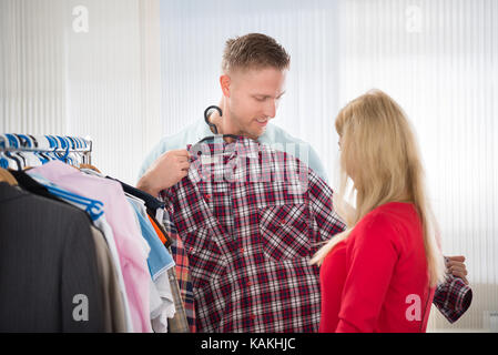 Giovane uomo che mostra controllato shirt per donna in negozio Foto Stock