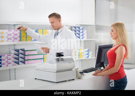 Il farmacista maschio dando lettura mentre la prescrizione di farmaci che dà al cliente femmina in negozio Foto Stock