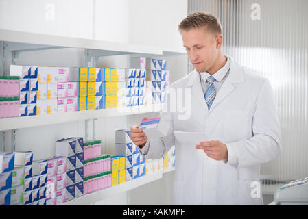 Il farmacista la lettura di etichetta sul pacchetto di medicina mentre si trattiene la carta di prescrizione in negozio Foto Stock