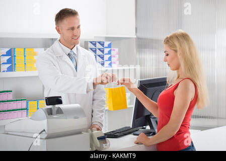 Sorridente al farmacista di dare medicine a femmina cliente al contatore in store Foto Stock