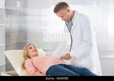 Medico maschio esaminando giovane donna incinta con uno stetoscopio in ospedale Foto Stock