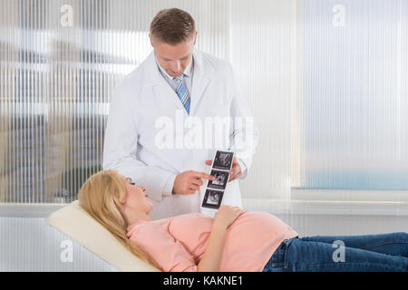 Giovane medico mostra di scansione ad ultrasuoni alla donna incinta in ospedale Foto Stock