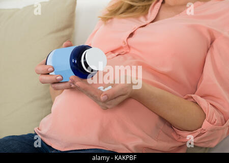 Sezione mediana della donna incinta versando pillole in mano dalla bottiglia in casa Foto Stock