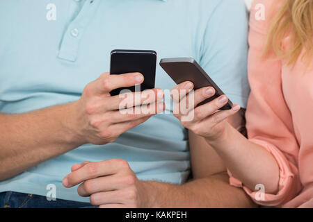 Sezione mediana della coppia giovane utilizzando i telefoni intelligenti per condividere i file Foto Stock