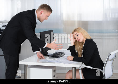 Boss grida al dipendente di sesso femminile seduto alla scrivania in ufficio Foto Stock