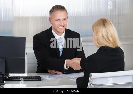 Sorridente giovane impreditore stringono le mani con il candidato donna alla scrivania in ufficio Foto Stock