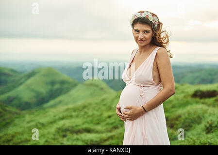 Incinta giovane donna indossa abbigliamento outdoor in naturale sfondo verde Foto Stock