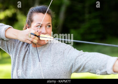 Atleta fiducioso puntando con arco e frecce nella foresta Foto Stock