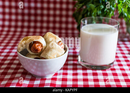 Piastra con mini hot dogs in casa (salsiccia in pasta) e un bicchiere di latte vaccino fresco con prezzemolo su un plaid sfondo. il 18 luglio, america celeb Foto Stock