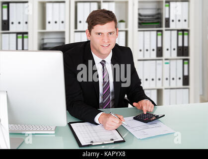 Ritratto di fiducioso ragioniere maschio utilizzando la calcolatrice a scrivania in ufficio Foto Stock