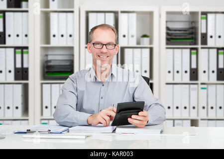 Ritratto di fiducioso coppia ragioniere utilizzando la calcolatrice per calcolare il finanziamento alla scrivania in ufficio Foto Stock