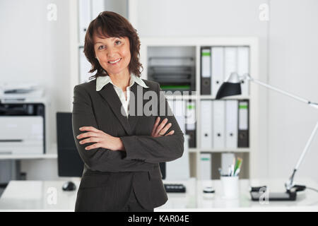 Ritratto di fiducioso imprenditrice matura in piedi con le braccia incrociate in office Foto Stock
