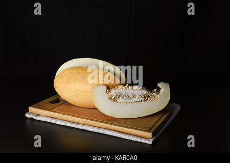 Melone e una fetta di melone su una tavola di legno su uno sfondo nero Foto Stock