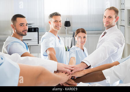 Ritratto di fiducioso team medico sorridere mentre unisce le mani in clinica Foto Stock