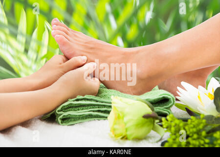 Immagine ritagliata della massaggiatrice massaggiare i piedi femminili contro foglie a beauty spa Foto Stock