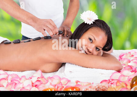 Ritratto di sorridente giovane donna getting hot stone therapy a spa salone Foto Stock