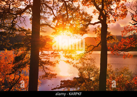 Friar's roccioso, Lake District. Sun scoppio attraverso le nuvole tra i picchi di Catbells, evidenziando il Fiery fogliame di autunno intorno Derwentwater. Foto Stock