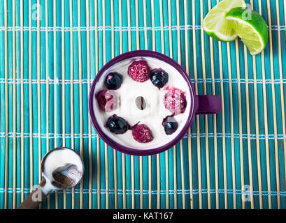 Lo yogurt greco con mirtilli e lamponi con succo di limone o di agrumi su un morbido rustico sfondo blu Foto Stock
