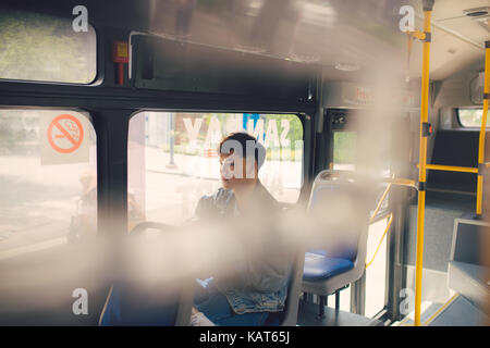 Giovane uomo asiatico sul tragitto in viaggio di lavoro seduti in autobus o in treno. Foto Stock