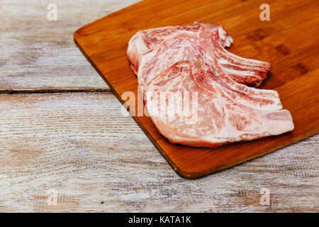 Materie bistecca di carne di maiale con il rosmarino pronto per la cottura di una bistecca di maiale su una tavola di legno Foto Stock
