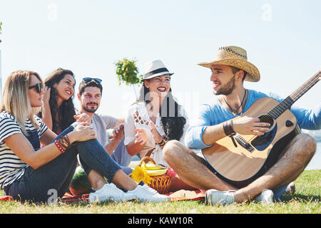 Felice giovani amici avente picnic nel parco.Essi sono tutti felici,avendo divertimento,sorridente e suonare la chitarra Foto Stock