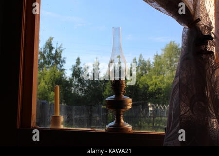 Una vecchia lampada di kerosene sorge su una tavola di legno davanzale. Foto Stock