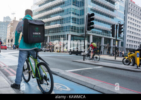 Un Uber mangia ciclista per la consegna al di fuori sede Uber in Aldgate Tower, Whitechapel, London, Regno Unito Foto Stock