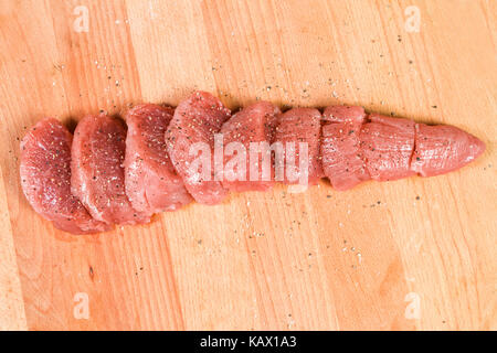 La carne cruda di filetti di maiale sul tagliere pronto per cuocere il filetto di maiale tagliato a pezzi di medaglioni marinato nel sale e pepe Foto Stock