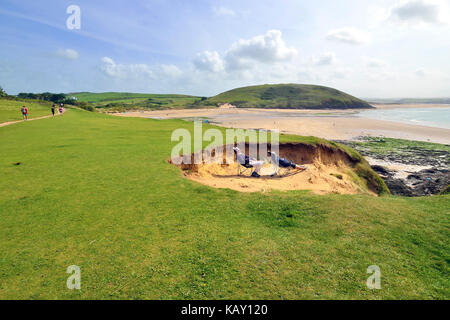 Uomo maturo e la donna riparo dal vento nelle dune di sabbia mentre crogiolandovi sotto i raggi del sole all'Daymer Bay, Cornwall, England, Regno Unito Foto Stock