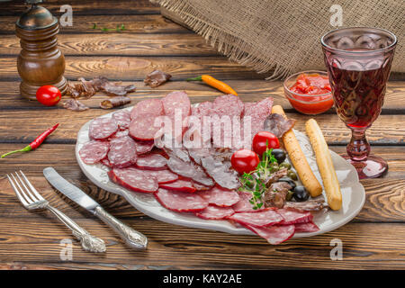 Antipasto a base di carne la selezione. Salame, prosciutto, grissini, olive e pomodori secchi, una glasse di vino rosso su sfondo di legno Foto Stock