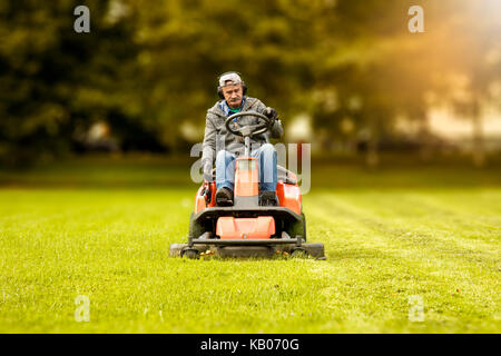 Il tosaerba aziona attraverso un verde prato Foto Stock