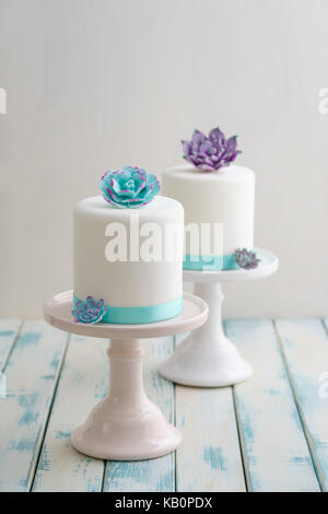 Due mini bianco torte nuziali covererd con fondente con pasta di gomma succulente su cavalletti di torta Foto Stock