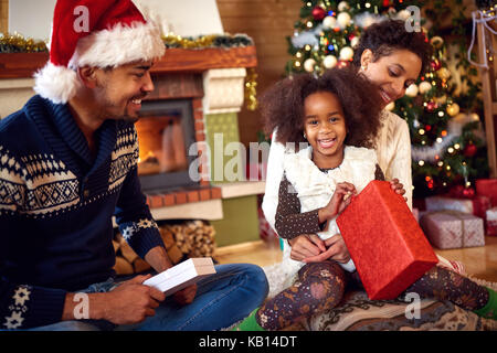 Molto bella sorridente ragazza nera con i genitori di aprire i regali di natale Foto Stock