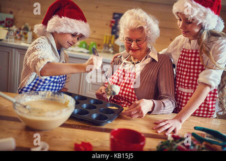 Nipoti godendo con la nonna la preparazione di biscotti di Natale a casa Foto Stock