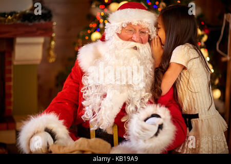 Babbo Natale e la bambina, natale scena. ragazza dire desiderio di santa claus l orecchio di fronte ad albero di natale Foto Stock