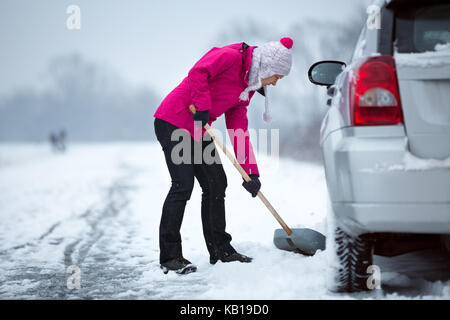 Donna con una pala la rimozione di neve attorno alla sua auto Foto Stock