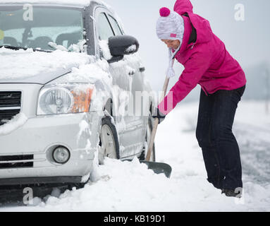 Donna con la pala si cancella la neve intorno alla macchina Foto Stock