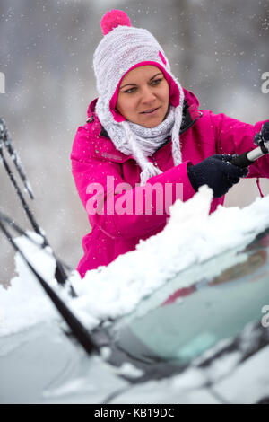 Ragazza giovane pulizia vetri auto da neve nella stagione invernale Foto Stock