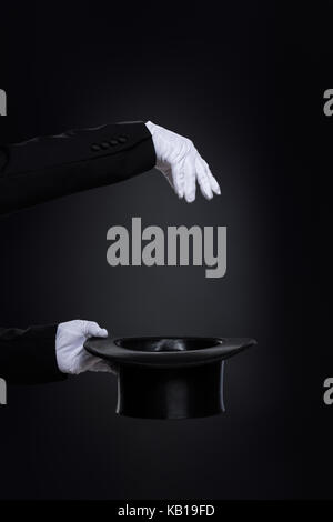 Magicianˈs mani in guanti bianchi con top hat sul nero Foto Stock