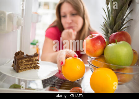 Donna titubante se mangiare pezzo di torta al cioccolato o arancio Foto Stock