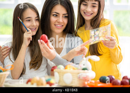 Madre e due ragazze rendendo la decorazione di pasqua in salotto luminoso Foto Stock