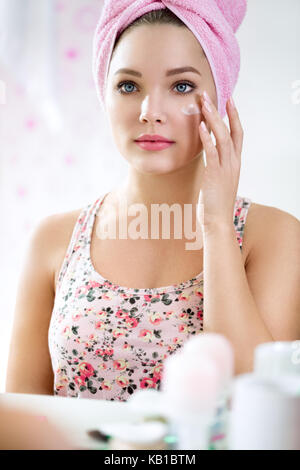 Giovane ragazza in bagno lato anteriore dello specchio retrovisore mettendo la crema, dermocosmesi Foto Stock