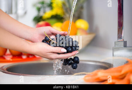 Donna di lavaggio mani un uva fresca sotto il rubinetto Foto Stock