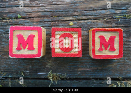 Per i bambini il giocattolo di legno blocchi MOM ortografia su uno spiovente di sfondo di legno. Foto Stock