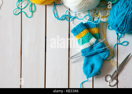 Una donna maglieria calze lavorate a maglia con bambini aghi di tessitura. strisce di turchese, giallo e bianco colori. Foto Stock